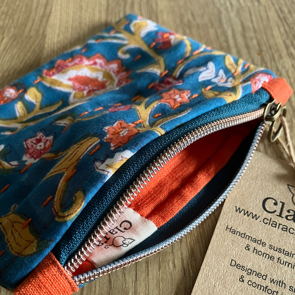 An individual handmade cotton and linen zipper pouch storage/purse, block printed by hand in teal blue with orange flowers, caramel foliage and an orange slow stitch embellishment, along with an orange lining. Sustainably made for your daily storage, essentials, toiletries, jewellery,  keys  and treasures.