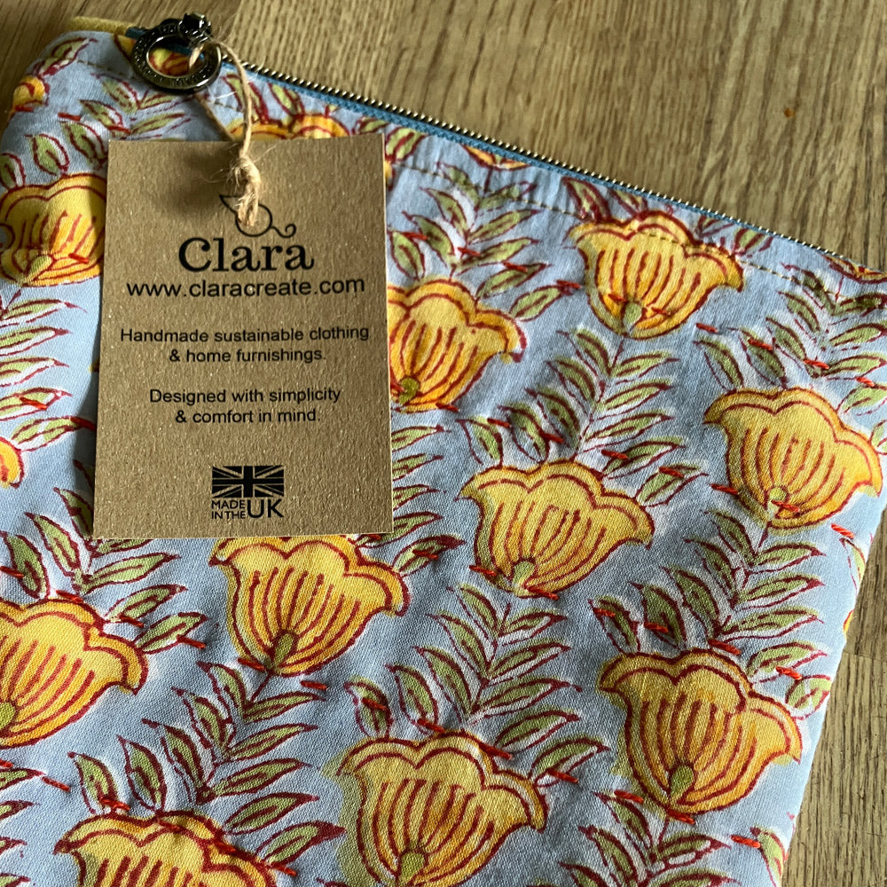 An individual cotton and linen zipper pouch bag, block printed by hand in light blue with gold flowers, green  foliage and slow stitch embellishment. Sustainably made for your daily storage, essentials, toiletries, jewellery, stationary or craft items and treasures.